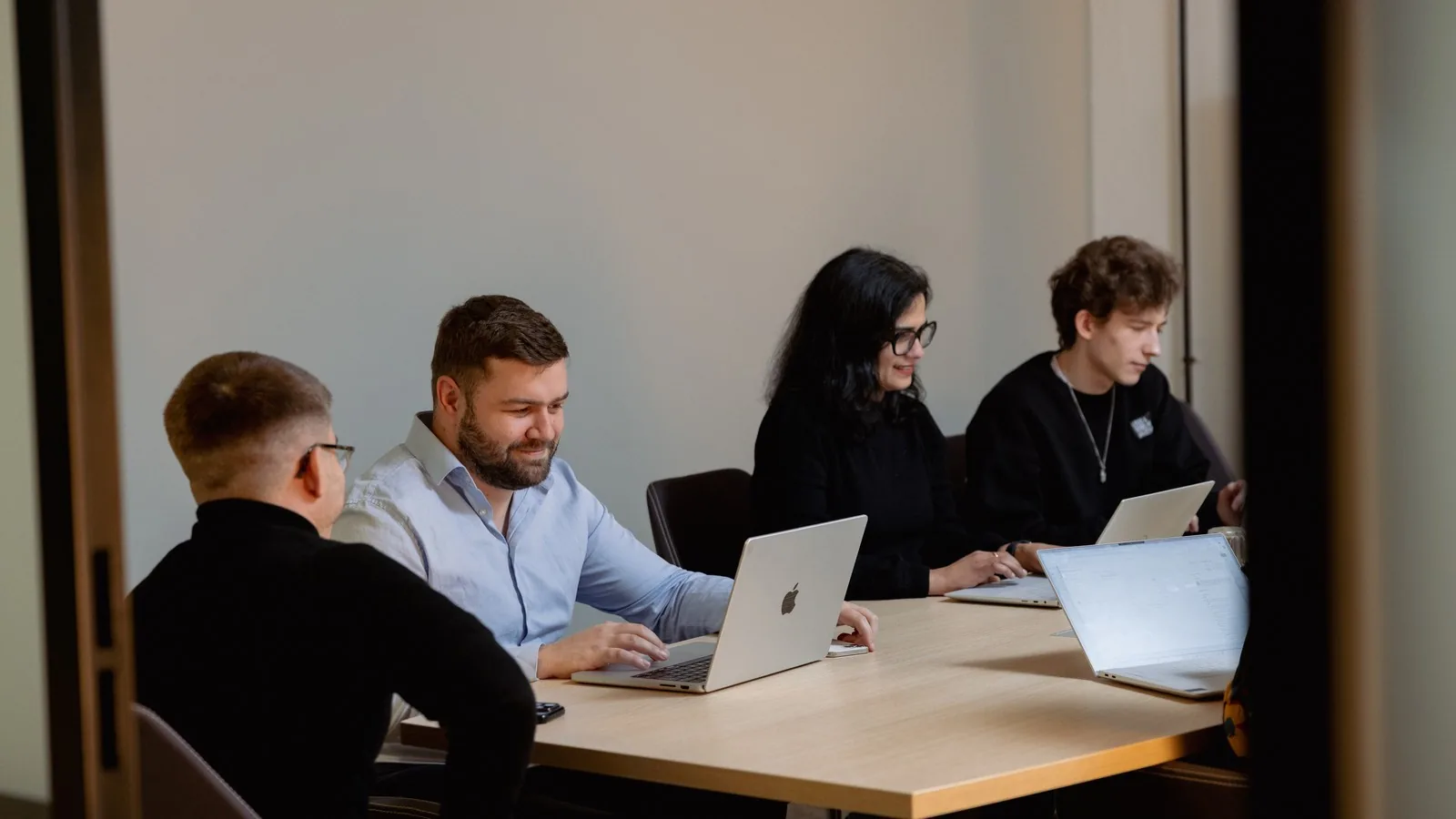 Vier collega&rsquo;s met laptops aan een tafel in een overleg